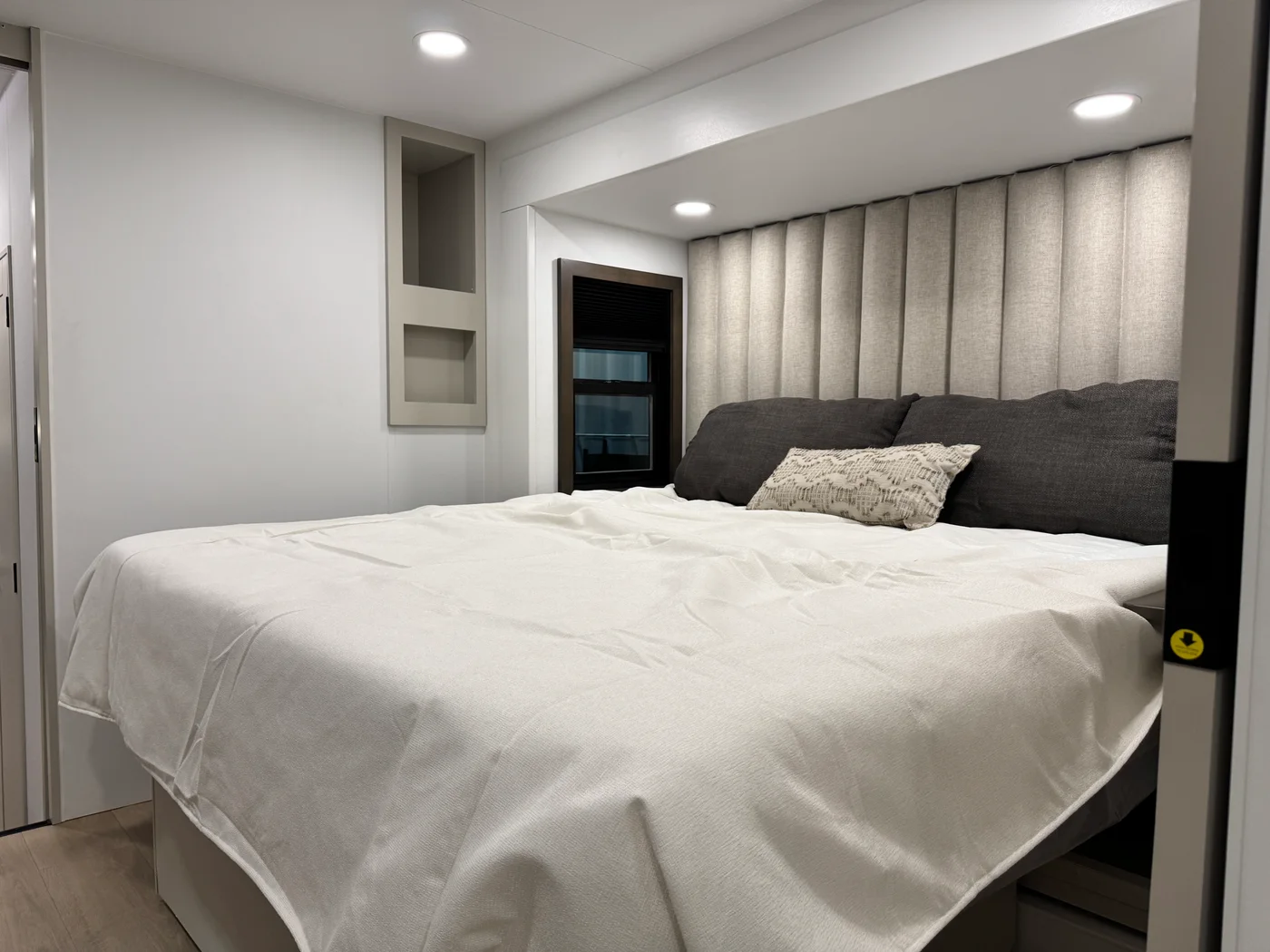 Aurum bedroom with a tall upholstered headboard, white bedding and bedside shelving.