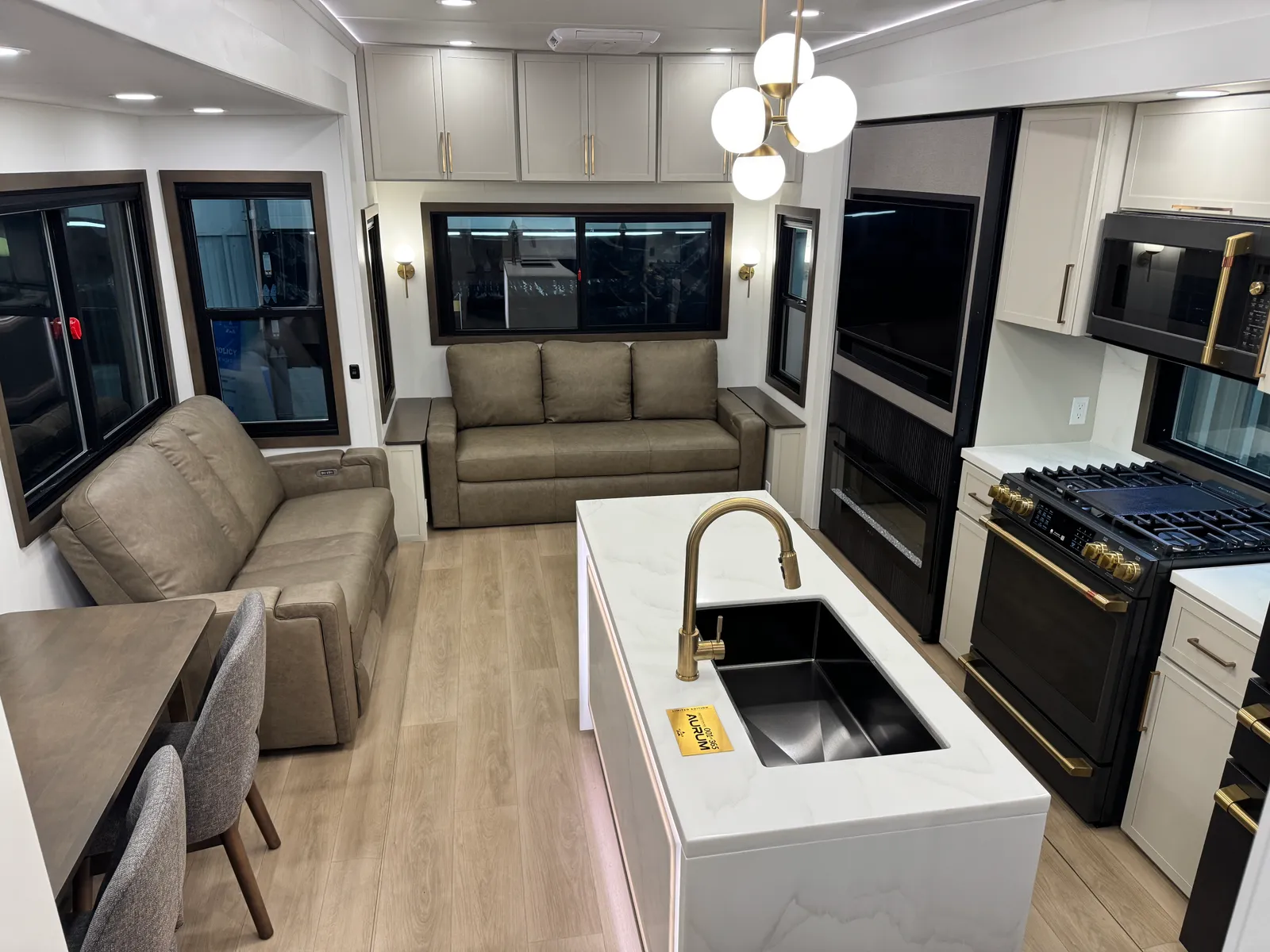 Interior view across the kitchen island, with a gold faucet, toward the dining table, sofa and range.