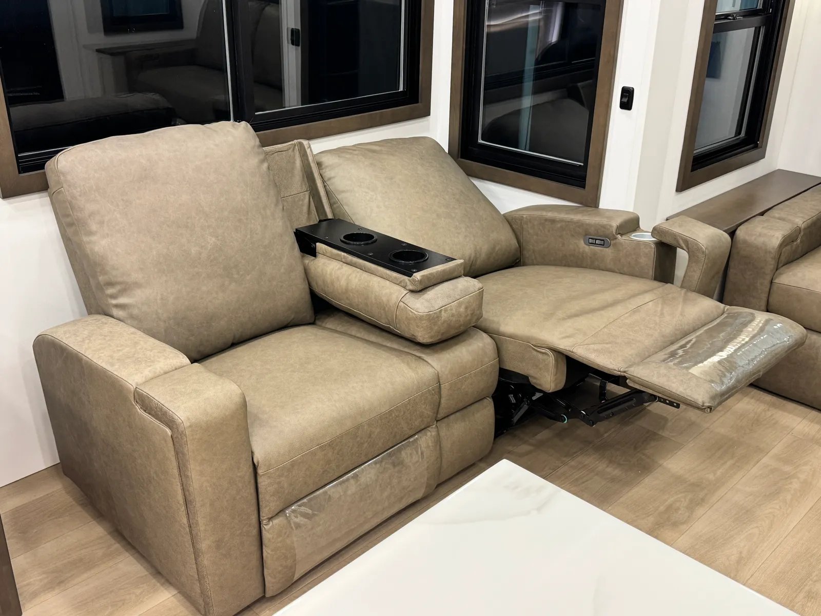 Leather theater seats with one footrest raised and a fold-down console with cupholders.