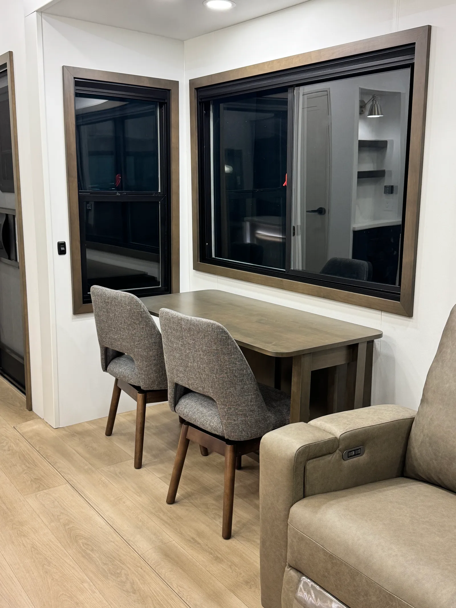 Wood dining table with two upholstered chairs beside two windows.