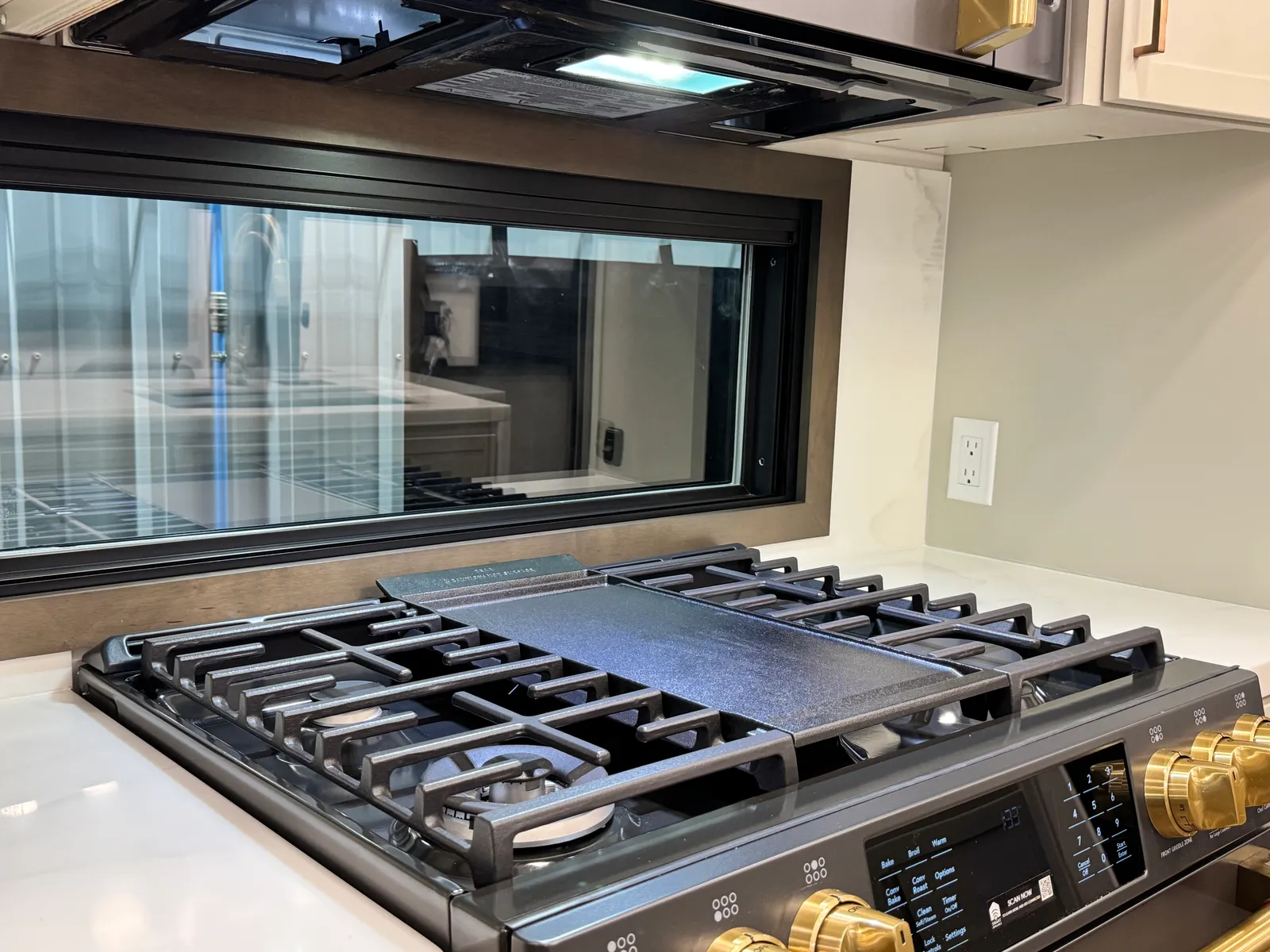 Gas cooktop with a griddle plate across the center burners and gold control knobs.