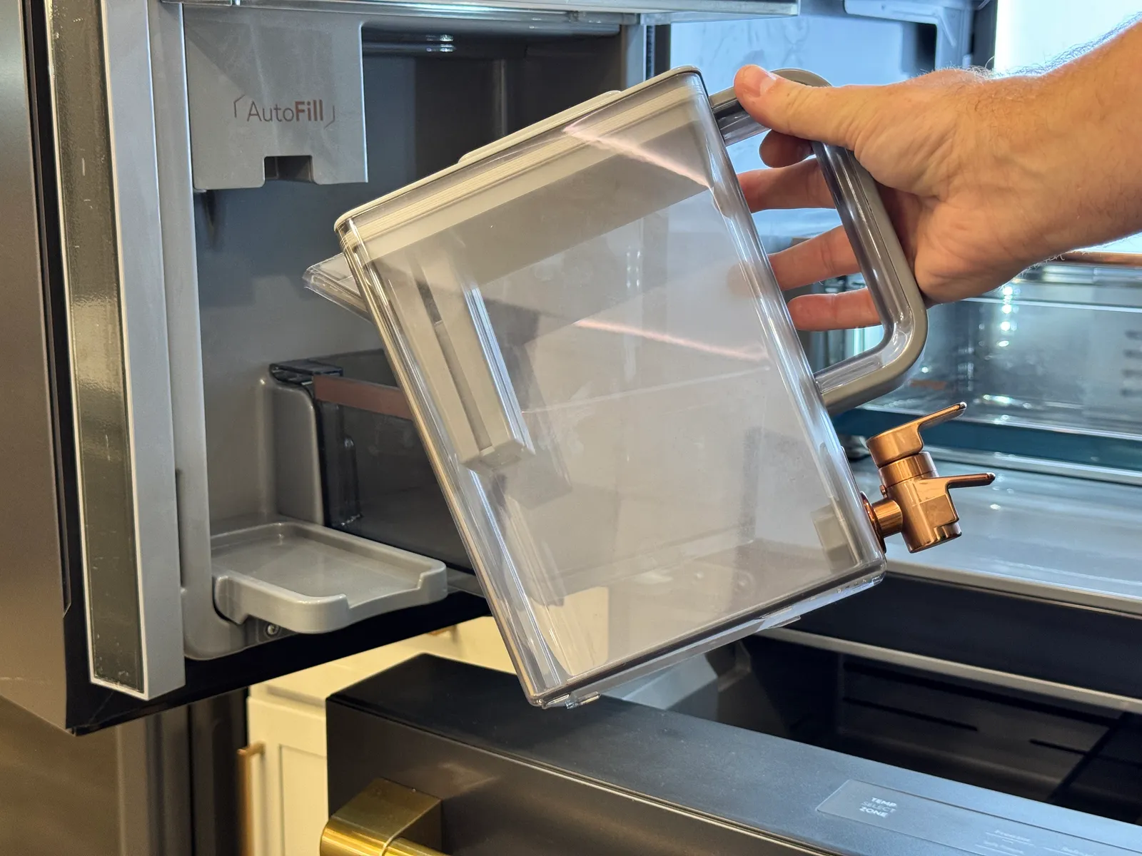 A hand lifting a clear water pitcher out of the refrigerator door.