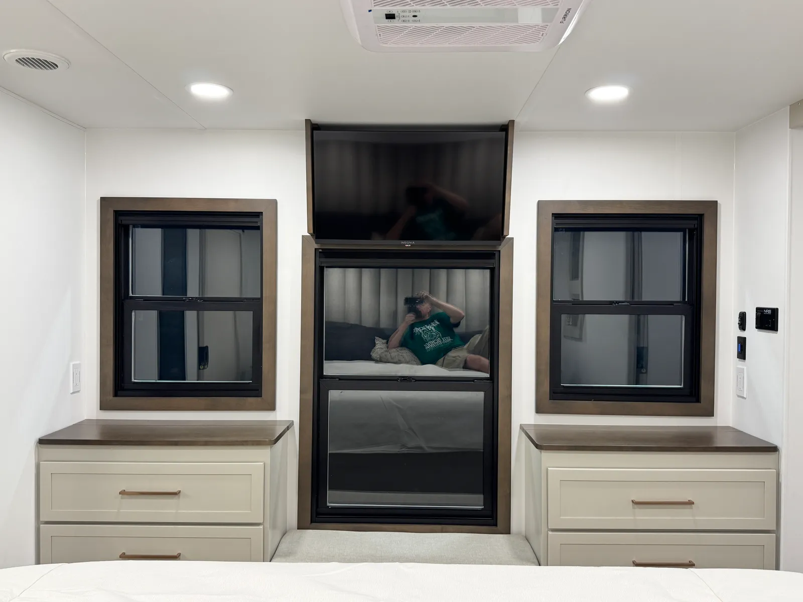 TV above a window at the foot of the bed, with dressers under the windows on either side.