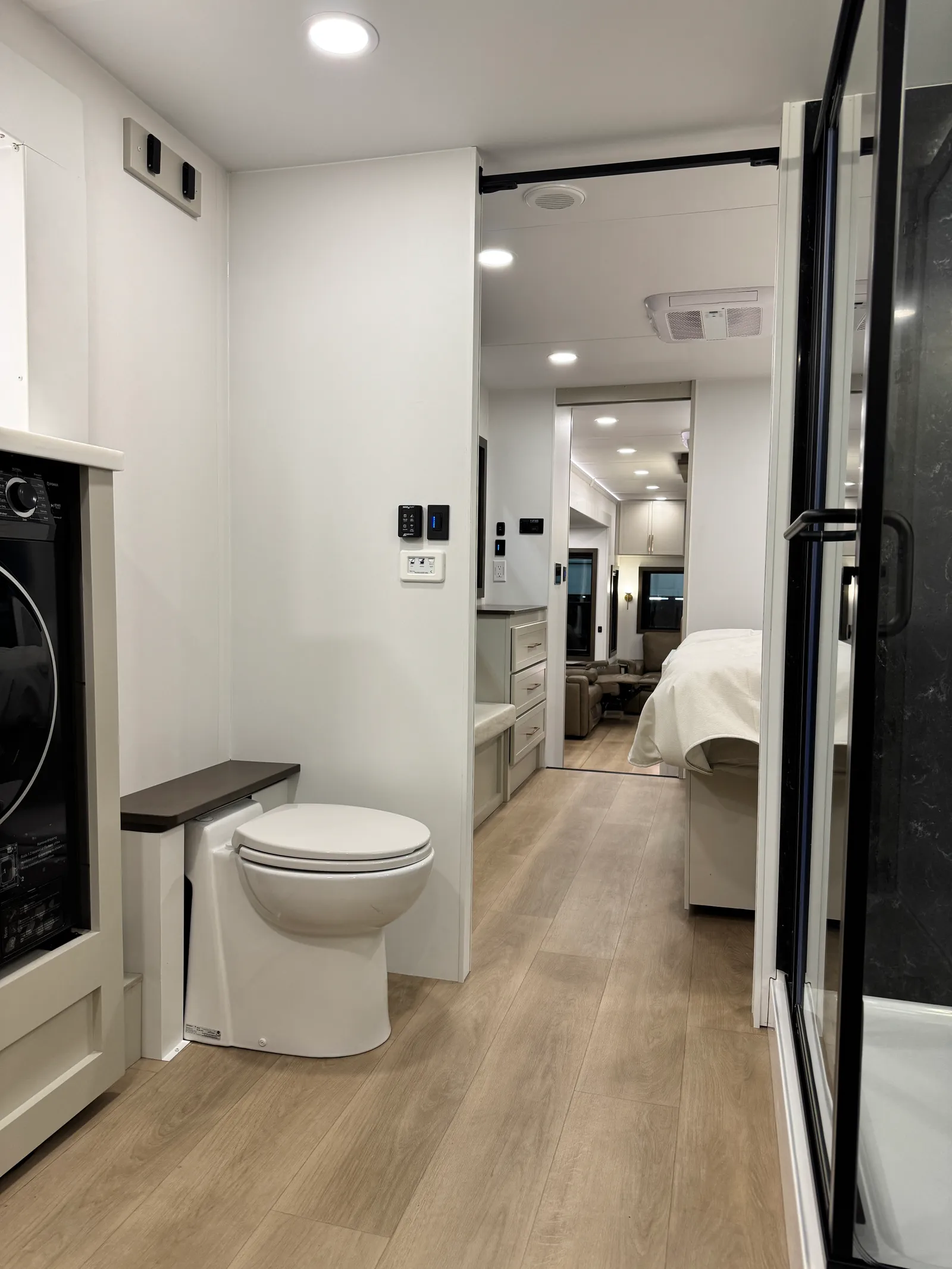 Front bath with a washer, a toilet and a glass shower door, looking back toward the bedroom.
