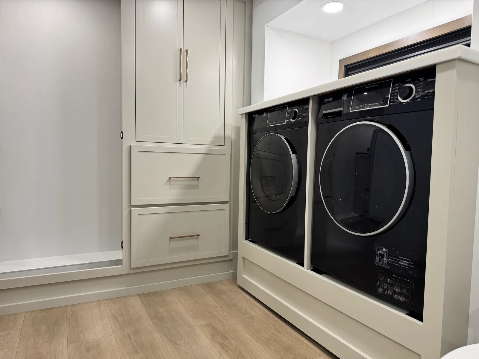 Side-by-side front-loading washer and dryer beneath a counter, next to tall cabinets.