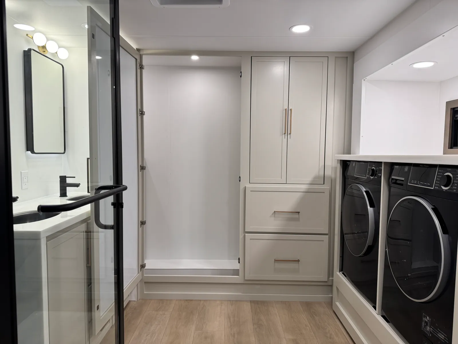 Washer and dryer beside a wardrobe cabinet, seen past the glass shower door.