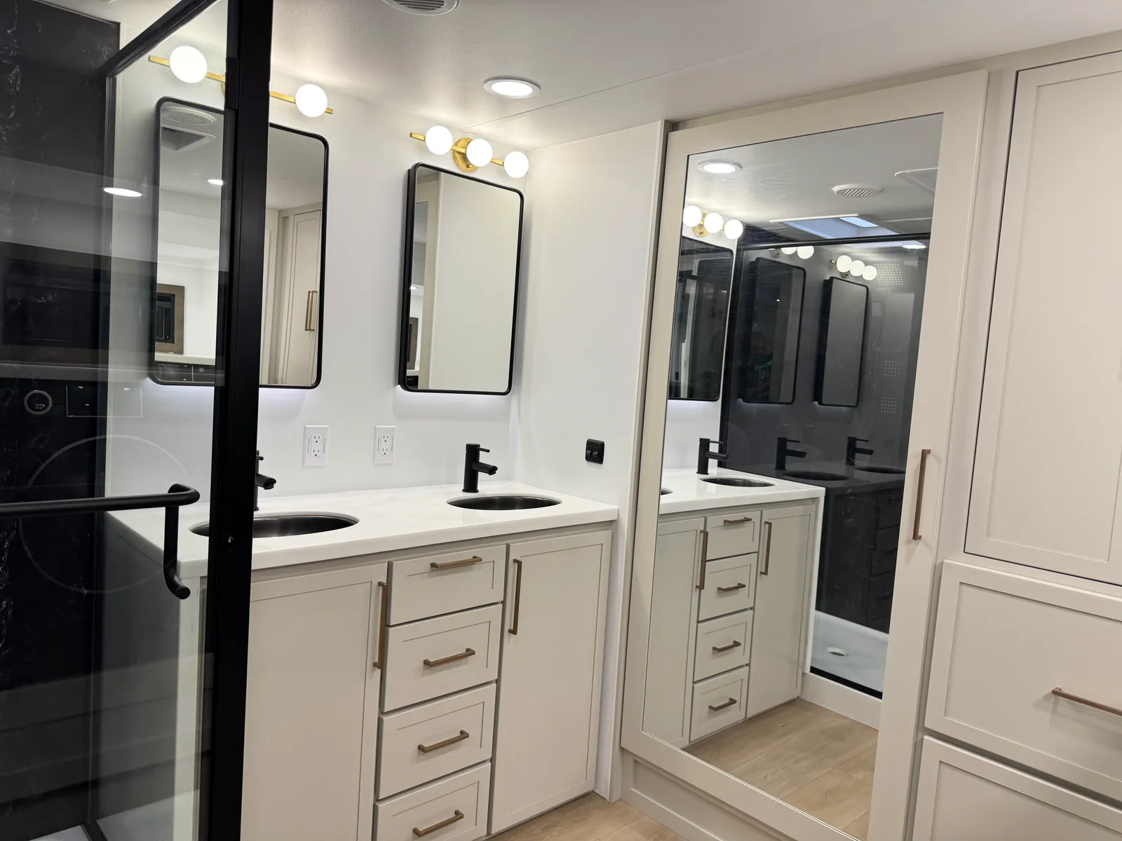 Two-sink vanity with black faucets and lighted mirrors, with the shower door at left.