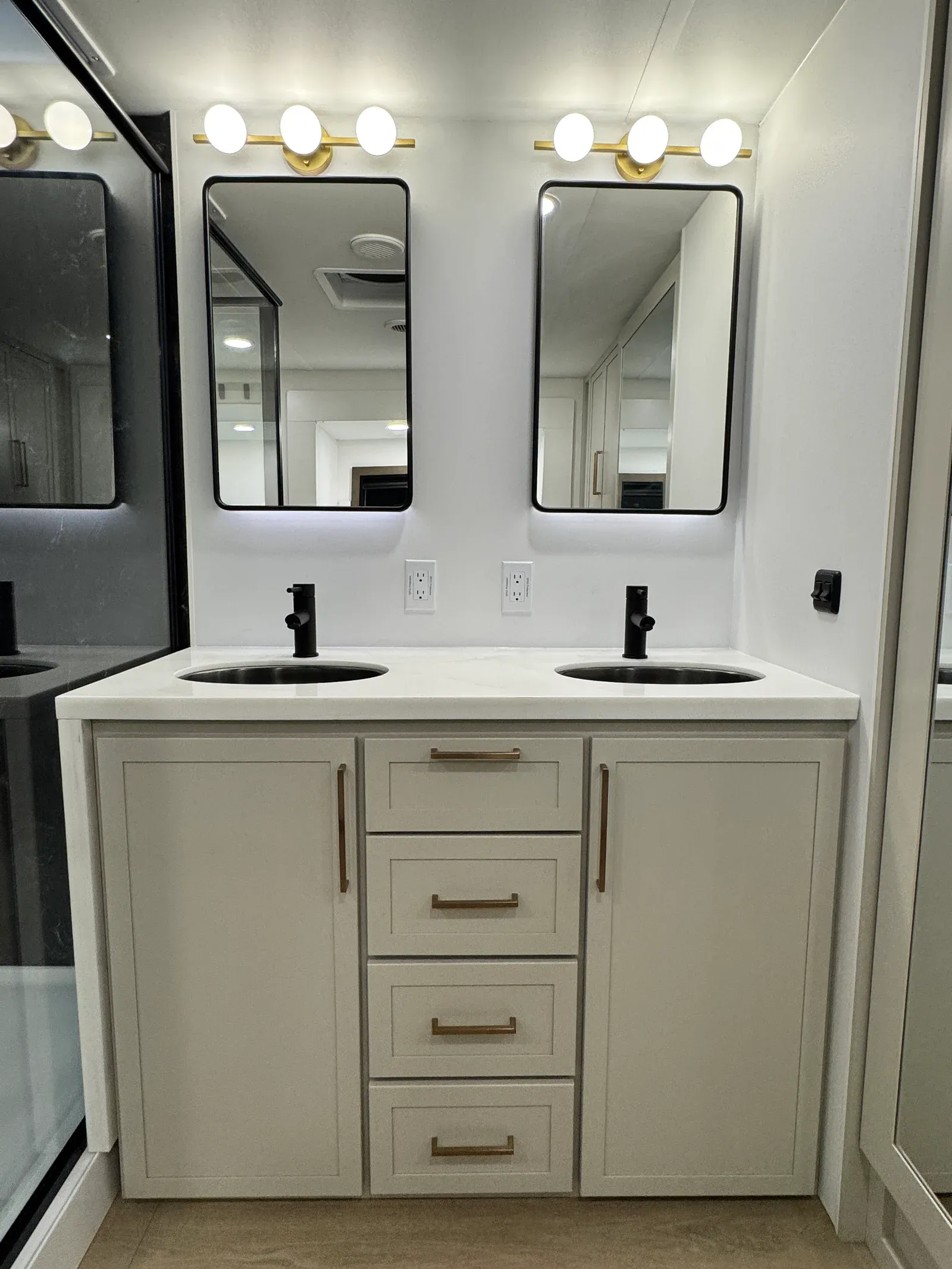 Straight-on view of the double vanity with drawers, two black sinks and gold light fixtures.