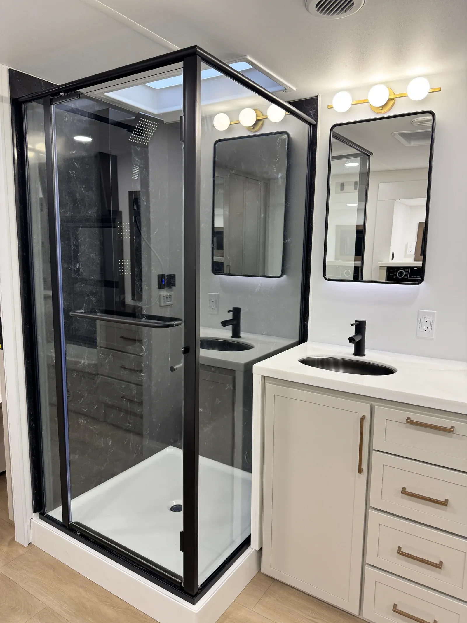 Glass-enclosed shower with black trim beside the vanity.