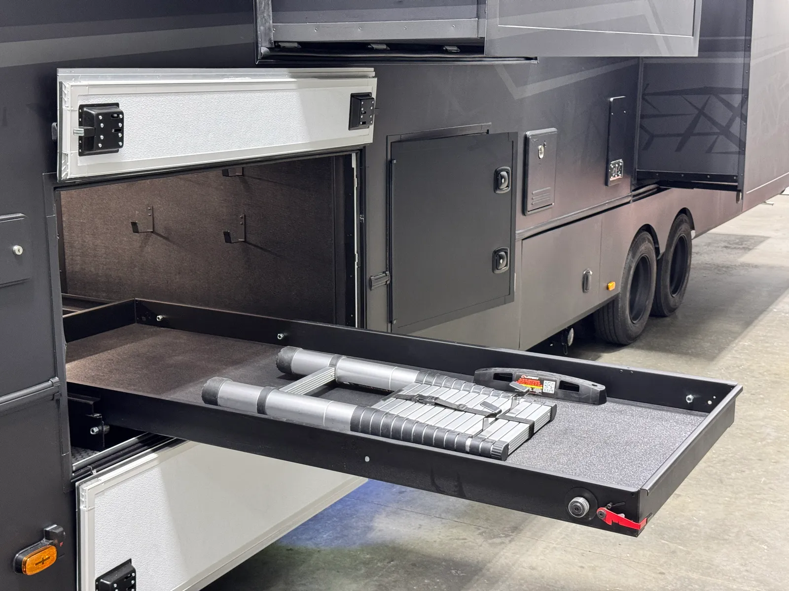 An exterior storage bay open with its tray slid out, holding folded gear.