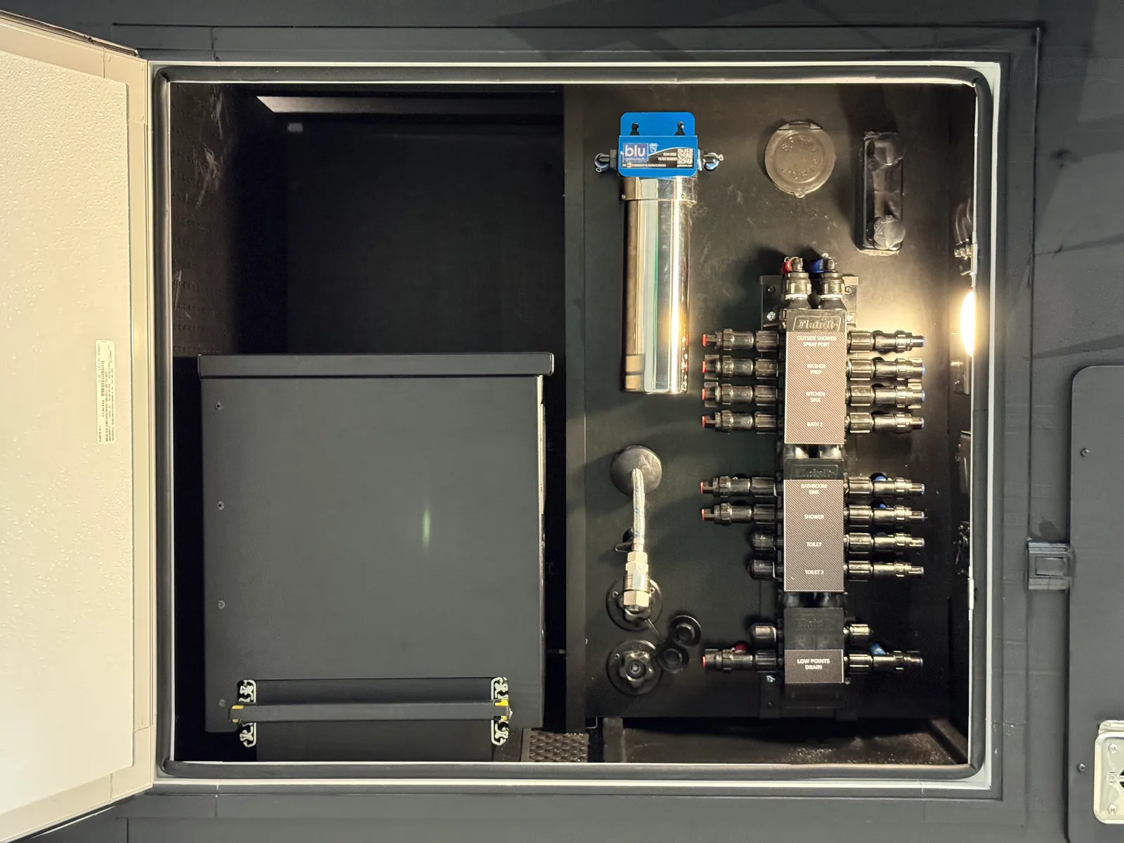 Utility bay with a labeled water manifold, a filter housing and a cabinet.
