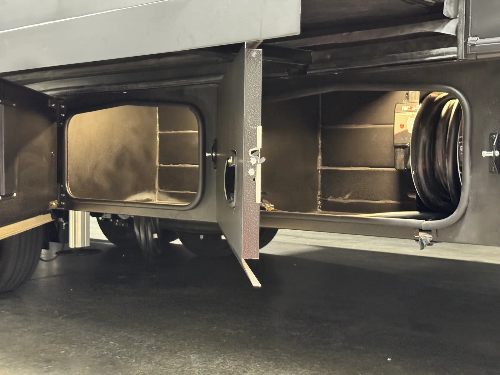 An open lower storage compartment next to a reel of black hose.