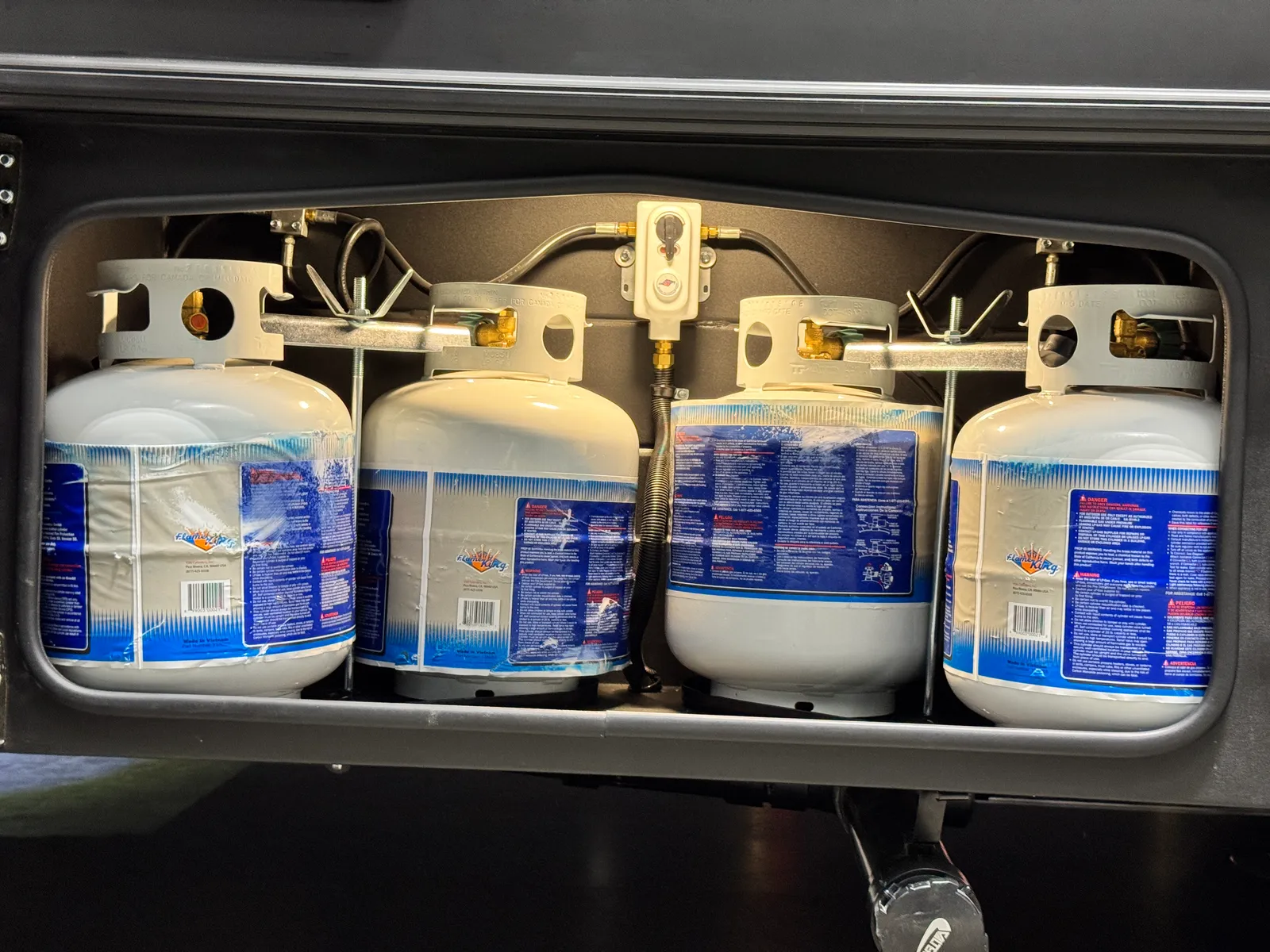 Four propane cylinders side by side inside an exterior compartment.