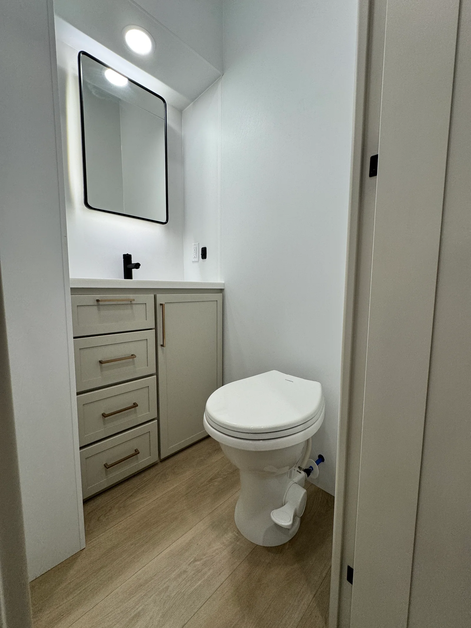 Separate half bathroom with a toilet, vanity, drawers and a lighted mirror.